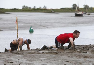 People crawling through the mud at the Maldon Mud Race, UK. To illustrate frustration at the lack of career progression within UK universities due to promotion freezes.