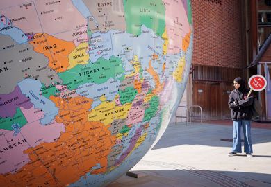 A student holds a Help paddle for those wanting advice during an open-day for prospective students alongside a sculpture of the world, London School of Economics, 9 April 2025. To illustrate international students.