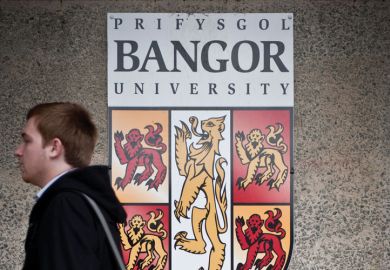 Student walking by Bangor University crest shield logo