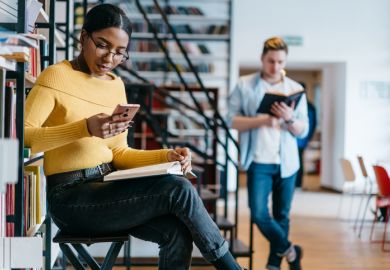 A female student on her phone while a male student reads a book