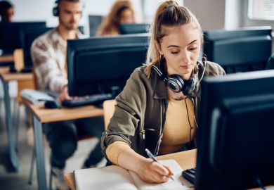 A university student writes notes while e-learning on a computer in the classroom