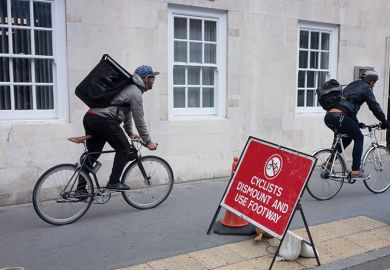 Two delivery couriers ignore a cyclist's dismount sign Two delivery couriers ignore a cyclist's dismount sign