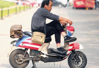 A Chinese man sits on a scooter decorated with America's Stars and Stripes outside a restaurant in Beijing on May 7, 2018. 