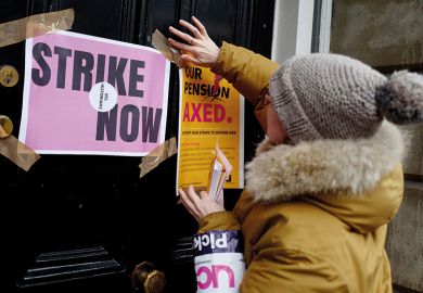 A demonstrator sticks a poster to a door as members of the University and College Union (UCU) stand at a picket line in protest against university lecturers' pay and pensions, outside of an entrance at University College London (UCL) in central London