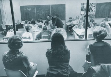 Three visiting teachers watch through a one-way window along the wall of a special demonstration classroom