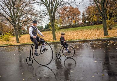 child rides past adult on high-wheel bicycles