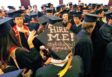 Graduating student displays a Hire me sign written on his mortar board