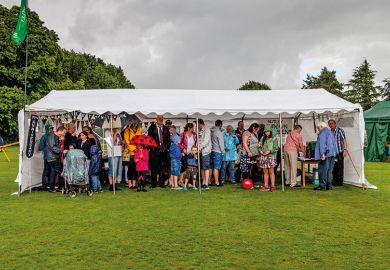 People standing under larger tent to shelter from rain