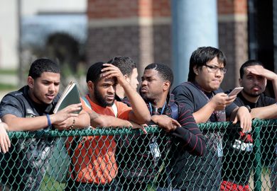 Students line the fence at the football field at university, USA 