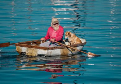An elderly man and his dog paddling a row boat in Monterey Bay, California. 
