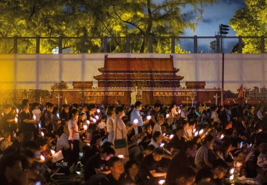People hold candles in front of a backdrop showing  Beijing's Tiananmen Square during a vigil in Hong Kong on June 4, 2018