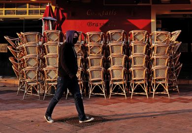 Man with facemask walking past closed cafe during coronavirus pandemic. France.