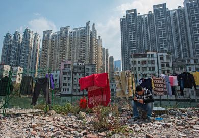 A man sits on a rock near demolished residential buildings in Xiancun, an urban village in the Zhujiang New Town district of Guangzhou as high commercial and residential buildings rise in the distance
