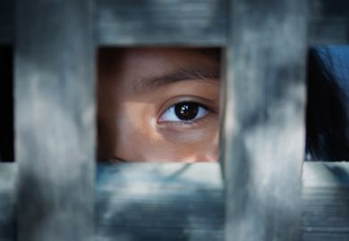 The blank stare of the eye of a child who is standing behind what appears to be a wooden frame illustrating modern slavery