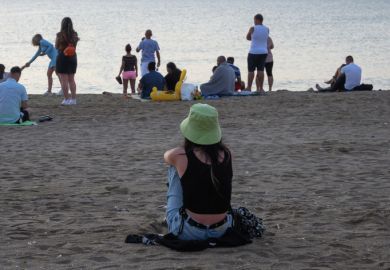 The young woman sits alone on the beach and admires the sea. In front of her are several people on the beach. Romania, Costinesti. August, 19, 2022