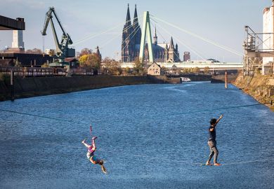 man and woman on slacklines in the Rhine harbour in Deutz, with the cathedral and Severins bridge in the background, Cologne, Germany, as a metaphor for European universities balancing cost and ambition