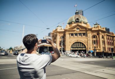  tourist is using his smart phone to take a photo of Flinders Street Train Station in Melbourne, Victoria