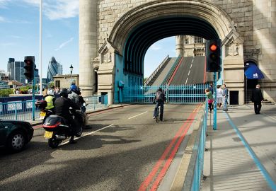 A cyclist, motorbikes and pedestrians wait as Tower Bridge in London is opened