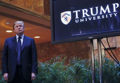 Donald Trump standing by a Trump University sign in New York City to illustrate Trump’s American Academy: pure politics, or valid idea?