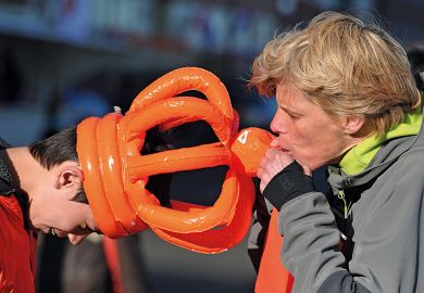 Person blows an inflatable orange crown to illustrate Universal exams can fix  the grade inflation crisis