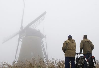 Two cyclists standing in fog looking at windmill