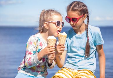 Two girls wearing eating ice cream on the seashore