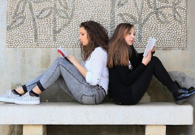 Two students sitting back to back reading books