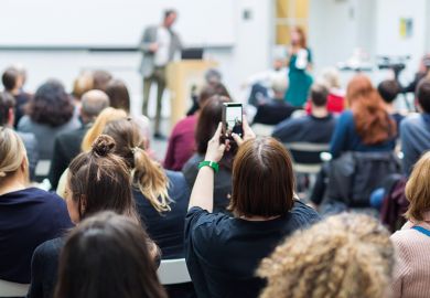 Student holding up phone in lecture. To illustrate concern about views expressed in class being shared on social media.