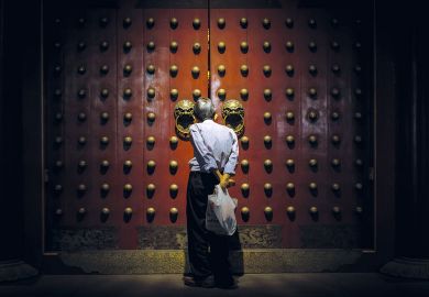 A person looks though the gap in the Buddhist temples giant red doors to illustrate Scholar ‘disinvited’ from conference ‘over husband’s activism’