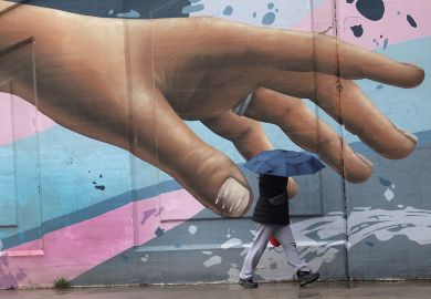 Wall art of hand reaching out with person walking by holding an umbrella in Toronto Wall art of hand reaching out with person walking by holding an umbrella in Toronto to illustrate How to meet  students’ soaring mental health  needs on a budget