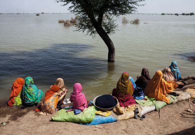 A group of women watch the floodwaters slowly rise to illustrate West’s ‘self-imposed boundaries’ hinder Pakistan