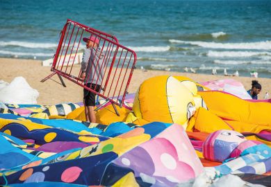 Man at work holding a gate walking on deflated balloons on Bournemouth beach in Dorset, England, UK. Man at work holding a gate walking on deflated balloons on Bournemouth beach in Dorset, England, UK.to illustrate Commit now to restoring ‘£7,000’ pension losses, say USS members