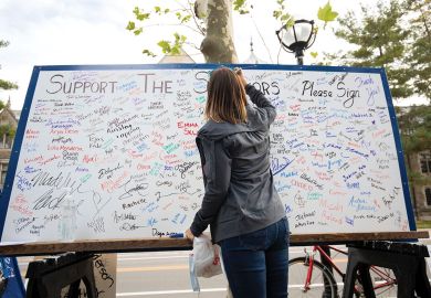 A woman signs a board in support of survivors of sexual abuse at a vigil in front of the home of outgoing University of Michigan President Mark Schlissel to illustrate the story 