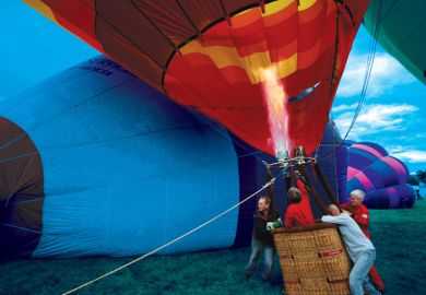 Balloonists hold down a basket as hot-air balloons begin to rise to illustrate Rising inflation will ramp up stratification in higher education