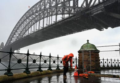 A construction worker sweeps away water while it rains next to the Harbour Bridge in Sydney to illustrate Shortened work rights ‘complicate’ skills drive