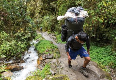 Hiker carrying enormous load on his back in the forest as a metaphor on the inexcusable fees levied on doctoral students.