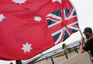 Person holding an upside down Red Ensign flag in Australia. Person holding an upside down Red Ensign flag in Australia as a metaphor that legal academics say ‘Top-down’ rules won’t solve free speech fears.