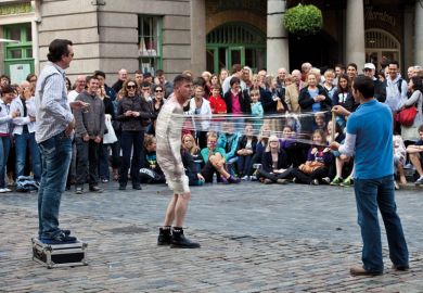 Street Entertainer unwrapping a person wrapped in cling film in Covent Garden, London to illustrate Problem of prestige dogs interdisciplinary campus