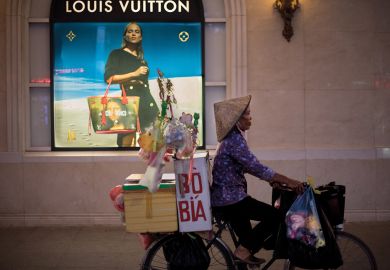 A bicycle vendor offering her merchandise in the streets of Hanoi pedals past a high end merchandise mall in the center of the city to illustrate Cost ‘barrier’ for Vietnam branch campuses under revised rules