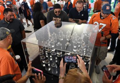 Football fans take a peek at Super Bowl rings in a glass display case to illustrate they are looking at  a 'small piece of excellence' which resembles the university as the university teaches in a research base approach producing high qualit