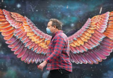Man with a mask walks in front of wings painting on wall Man with a mask walks in front of wings painting on wall as a metaphor for Which Covid innovations should be embraced
