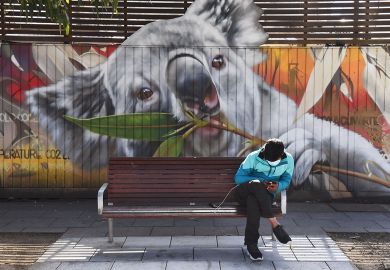 A man looks at his phone as he sits in front of a mural of a koala in Melbourne to illustrate Economic changes ‘slowing Australian students down’