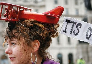 A protestor wears a toy aeroplane on her head with a banner reading  'It's over' A protestor wears a toy aeroplane on her head with a banner reading  'It's over' to illustrate  ‘Set institutional carbon budgets to cut flying and support rail travel’