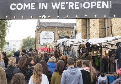 crowds passing under an entrance sign reading " Come in We're (very) Open.