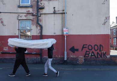 Two men carry a mattress over their heads past a terraced house, the walls of which bare graffiti reading "food bank"  Two men carry a mattress over their heads past a terraced house, the walls of which bare graffiti reading "food bank" to illustrate Cost of living crisis bites for PhDs on ‘inadequate’ stipends