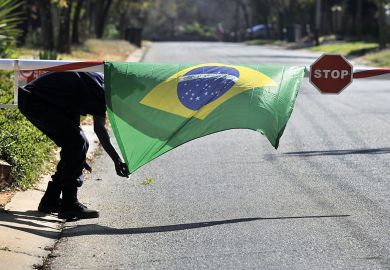 A security guard tries to tie down a Ukraine-flag over a stop sign on a barrier to illustrate Open access is closed to middle-income nations too rich for fee waivers