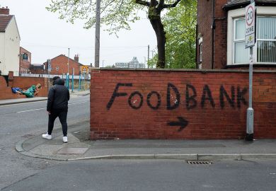 Person passes by bold, black graffiti that points towards a local food bank to illustrate that One in four UK universities now running a food bank