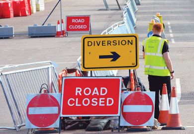 Worker standing with no entry, diversion and road closed  road-signs Worker standing with road-signs as a metaphor for shortages at labs caused by border snarls and new rules.