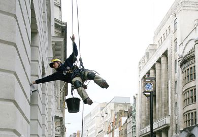 Image of a man suspended from ropes cleans an office in central London as metaphor for that universities in London will be tipped into deficit or pushed further into the red