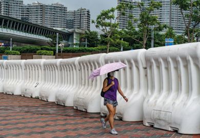 A woman holding an umbrella walks in front of a line of barriers at soutside the West Kowloon A woman holding an umbrella walks in front of water barrier soutside the West Kowloon